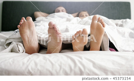 Young loving joyful couple playing and dancing their feet under blanket while wake up in bed in the 45373154
