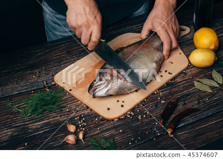 male chef cuts raw trout on a wooden Board in the kitchen. Raw fish for cooking male chef cuts raw trout on a wooden Board in the kitchen. Raw fish for cooking 45374607