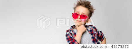 A handsome boy in a plaid shirt, gray shirt and jeans stands on a gray background. A boy in red A handsome boy in a plaid shirt, gray shirt and jeans stands on a gray background. A boy in red 45375272