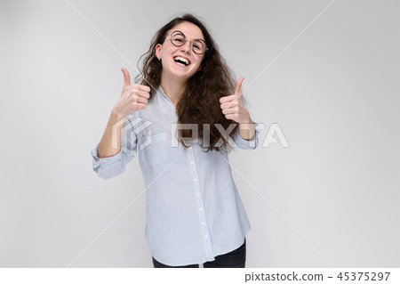 Portrait of a young girl in glasses. Beautiful young girl on a gray background. The girl shows the 45375297