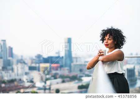 A portrait of a woman standing on a terrace, holding a cup of coffee. 45378856