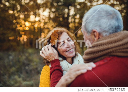 A senior couple standing in an autumn nature at sunset, looking at each other. 45379285