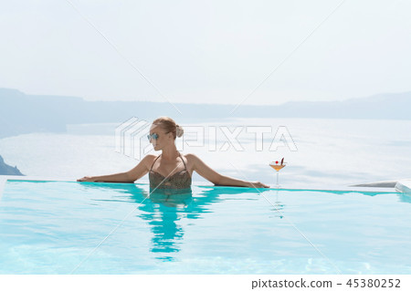 Young woman relaxing in the pool with a gorgeous view on Santorini. 45380252