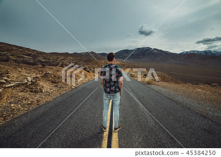 Man standing on empty desert asphalt road waiting  45384250