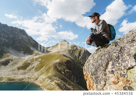 A bearded hipster tourist in sunglasses with a backpack sits on the edge of a cliff high in the A bearded hipster tourist in sunglasses with a backpack sits on the edge of a cliff high in the 45384538