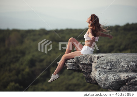 woman sitting on the rock cliff with hands raised woman sitting on the rock cliff with hands raised 45385899