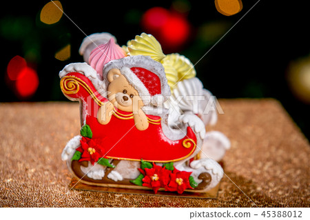 Gingerbread sleigh with teddy bear in front of defocused lights of Christmas decorated fir tree 45388012