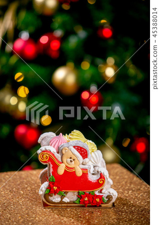 Gingerbread sleigh with teddy bear in front of defocused lights of Christmas decorated fir tree 45388014