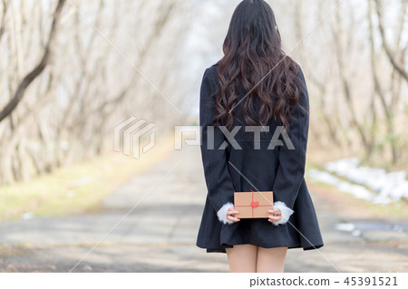 Young woman with present box behind hand 45391521