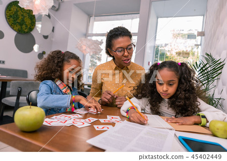 Helpful smart nursery teacher wearing glasses teaching two girls letters Helpful smart nursery teacher wearing glasses teaching two girls letters 45402449