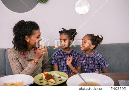 Caring loving curly mother giving some cheesecake her cute little girls Caring loving curly mother giving some cheesecake her cute little girls 45402595