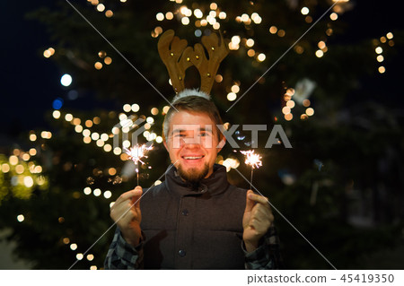 People, holidays and christmas concept - surprised man in deer's horns holding two bengals light or 45419350