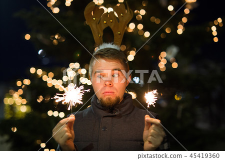 People, holidays and christmas concept - surprised man in deer's horns holding two bengals light or 45419360