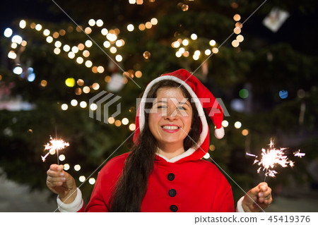 People, holidays and christmas concept - young woman in Santa costume with sparklers or Bengal light 45419376