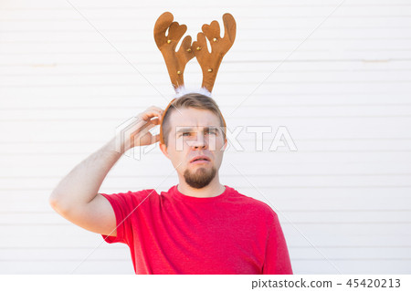 Christmas, holidays and people concept - a man's head with deer horns on it. Man scratches his head Christmas, holidays and people concept - a man's head with deer horns on it. Man scratches his head 45420213