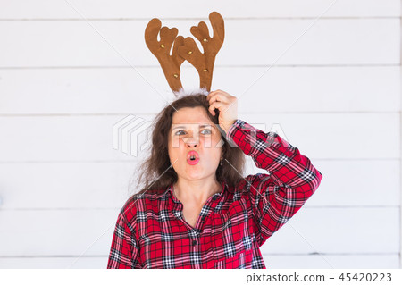 Christmas, holidays and people concept - a woman's head with deer horns on it. Woman scratches her Christmas, holidays and people concept - a woman's head with deer horns on it. Woman scratches her 45420223