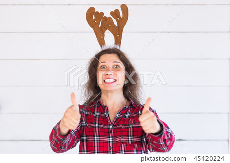 Happy beautiful woman in Christmas costume with deer horns on her head gesturing thumbs up over 45420224