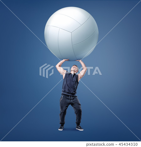 A small muscular athlete holds a large white volleyball ball on straight arms above himself. A small muscular athlete holds a large white volleyball ball on straight arms above himself. 45434310