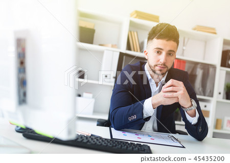 A young man sitting in the office at a computer Desk and working with documents. A young man sitting in the office at a computer Desk and working with documents. 45435200