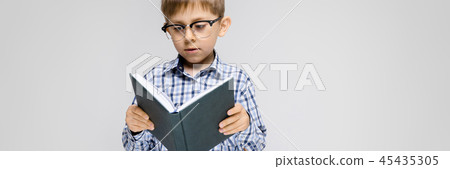 A charming boy with an inlaid shirt and light jeans stands on a gray background. The boy is holding A charming boy with an inlaid shirt and light jeans stands on a gray background. The boy is holding 45435305