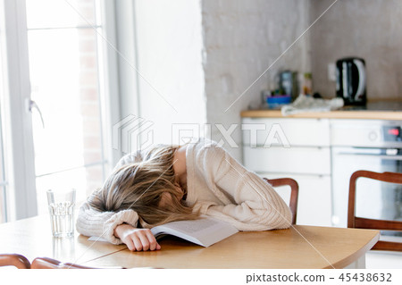 Tired girl in white sweater with book at kitchen Tired girl in white sweater with book at kitchen 45438632
