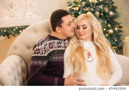 Yong fimily in beautiful knitted sweaters in Christmas holidays sits on sofa in front of Christmas 45442004