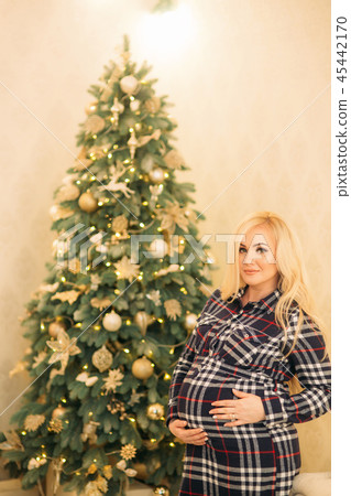 A beautiful pregnant blonde girl decorates a Christmas tree with beautiful toys. Christmas mood A beautiful pregnant blonde girl decorates a Christmas tree with beautiful toys. Christmas mood 45442170