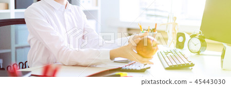 A young girl at the office is working with documents and stretches forth an apple. 45443030