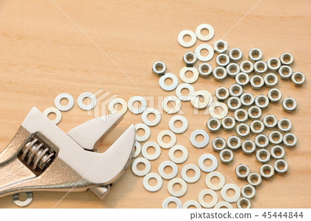 Monkey wrenches with numerous hex nuts and washers placed on a wooden board. 45444844