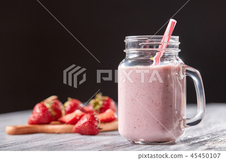 Homemade strawberry milk shake in a jar with a straw on a wooden table around a black background 45450107