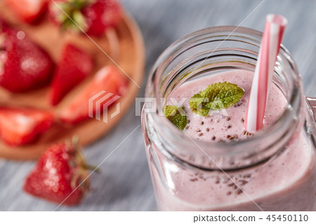 Closeup of organic milky strawberry smoothie with chia seeds and mint leaves in a glass with a straw 45450110