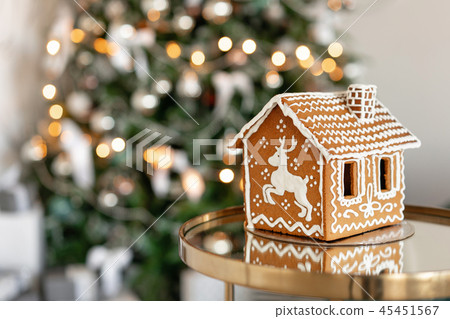 Gingerbread house on table. Defocused lights of Christmas tree. Morning in the bright living room Gingerbread house on table. Defocused lights of Christmas tree. Morning in the bright living room 45451567