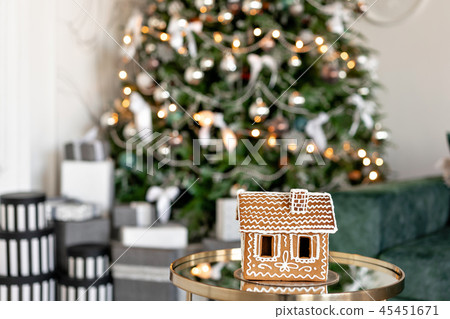 Gingerbread house on table. Defocused lights of Christmas tree. Morning in the bright living room Gingerbread house on table. Defocused lights of Christmas tree. Morning in the bright living room 45451671