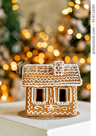 Gingerbread house on table. Defocused lights of Christmas tree. Morning in the bright living room Gingerbread house on table. Defocused lights of Christmas tree. Morning in the bright living room 45451680