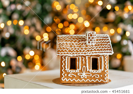 Gingerbread house on table. Defocused lights of Christmas tree. Morning in the bright living room Gingerbread house on table. Defocused lights of Christmas tree. Morning in the bright living room 45451681