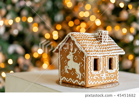 Gingerbread house on table. Defocused lights of Christmas tree. Morning in the bright living room Gingerbread house on table. Defocused lights of Christmas tree. Morning in the bright living room 45451682