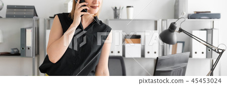A young girl standing in the office and talking on the phone. 45453024