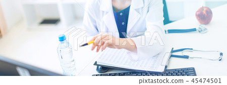 A beautiful young girl in a white robe is sitting at a computer desk with documents and a pen in her 45474501