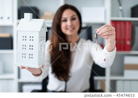 A young girl sitting at a table and holding a house and keys. A young girl sitting at a table and holding a house and keys. 45474653