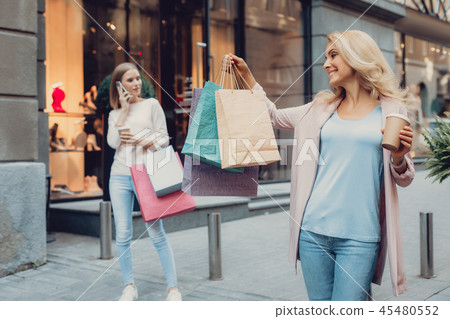 Charming lady looking at shopping bags while her daughter talking on cellphone Charming lady looking at shopping bags while her daughter talking on cellphone 45480552