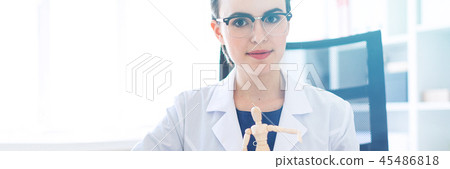 A beautiful young girl in a white robe is sitting at a table and holding a wooden figure of a man in 45486818