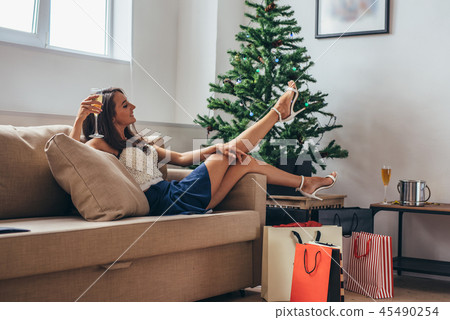 Woman siting by the christmas tree and taking a present out of shopping bag Woman siting by the christmas tree and taking a present out of shopping bag 45490254