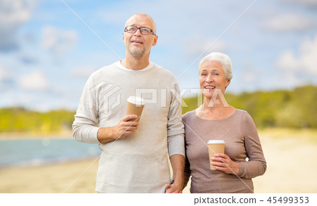 senior couple with takeaway coffee on beach 45499353
