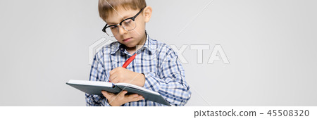 A charming boy with a vkletchatoy shirt and light jeans stands on a gray background. The boy holds a 45508320