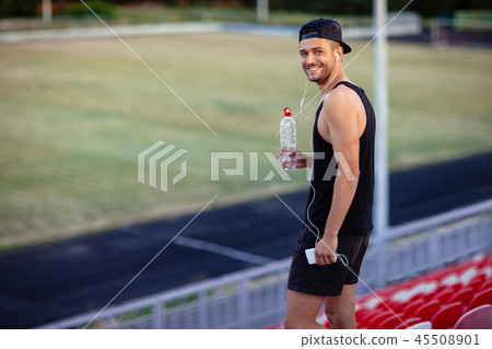 Handsome happy man with bottle of water, in headphones listening Handsome happy man with bottle of water, in headphones listening 45508901