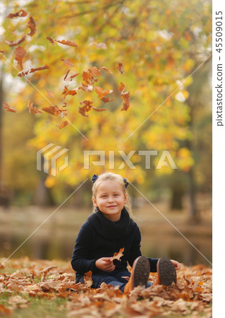 Beautiful young girl sist in leaves and throws them up. Colorful background. Happy little girl smile 45509015