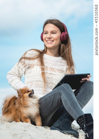 14 years girl in a wireless headphones listening to a music from a smart phone on a beach. against a 45510368