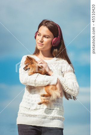 14 years girl in a wireless headphones listening to a music from a smart phone on a beach. against a 45510420
