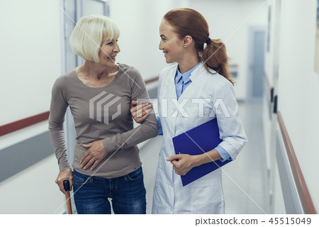 Merry doctor is leading woman with cane through clinic 45515049