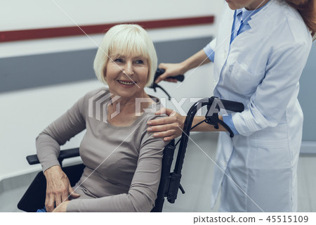 Female practitioner is propelling happy disabled lady in clinic Female practitioner is propelling happy disabled lady in clinic 45515109